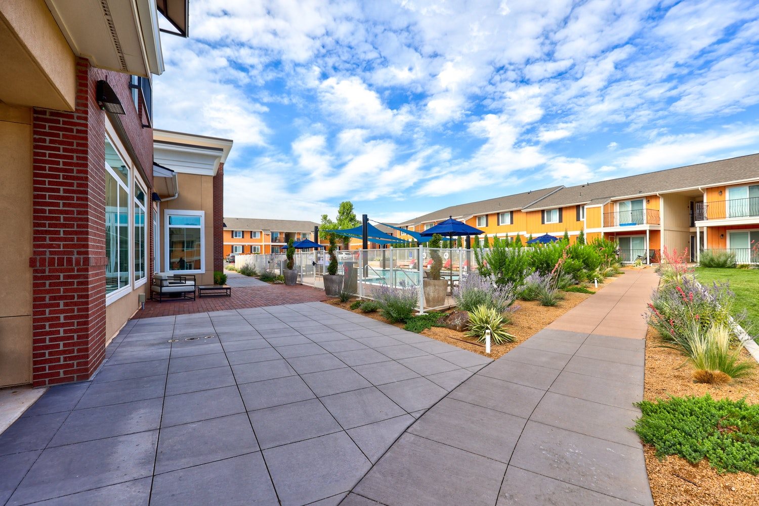 A long concrete walkway leads to a building with a brick wall on the left.